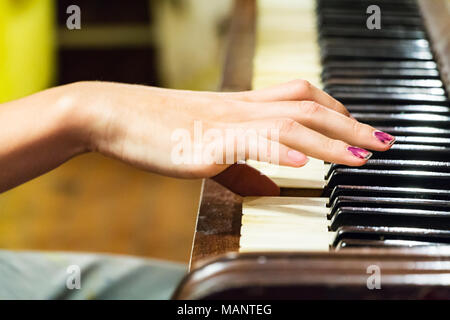 Una mano di una femmina di giovane donna con unghie colorate giocando molto vecchio pianoforte con tasti in avorio.