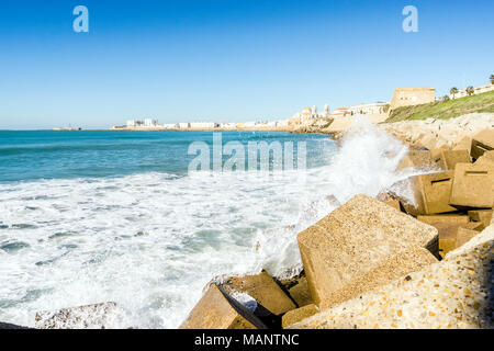 Atlantic di onde che si infrangono sulla riva urbanizzata di vecchi Cadice, Andalusia, Spagna Foto Stock