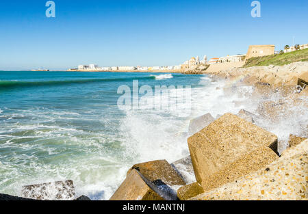 Atlantic di onde che si infrangono sulla riva urbanizzata di vecchi Cadice, Andalusia, Spagna Foto Stock