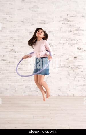 Ragazza energico il salto in aria con hula hoop in una luminosa camera spaziosa Foto Stock