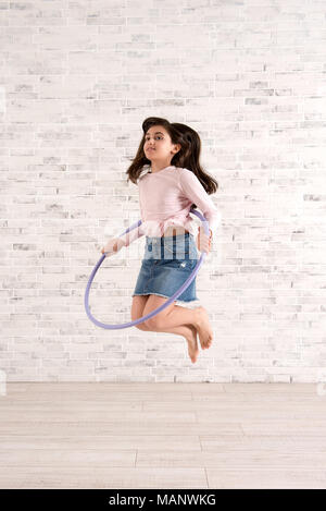 Vigorosa ragazza il salto in aria con hula hoop in una luminosa camera spaziosa Foto Stock