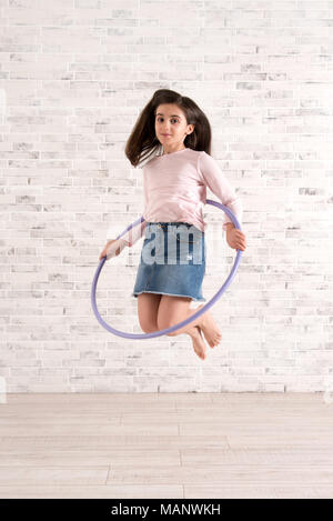 Giovane ragazza vigorosa il salto in aria con hula hoop in una luminosa camera spaziosa Foto Stock