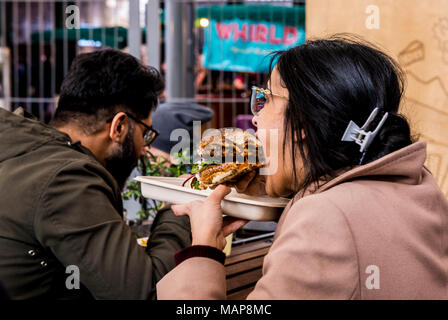 Donna di mordere in bun vicino vicino al Mercato di Borough, Southwark, Londra, Inghilterra, Regno Unito Foto Stock