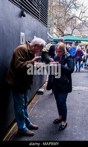 L uomo e la donna a mangiare cibo al di fuori del mercato di Borough, Southwark, Londra, Inghilterra, Regno Unito Foto Stock