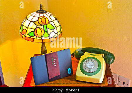 Comunicazioni vecchio e nuovo! Un telefono GPO risalente al 1972 (tipo 746F) si siede accanto a un moderno telecoms router, tutte sotto un retrò lampada Tiffany. Foto Stock