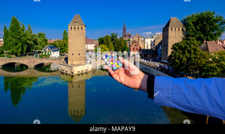 Mano che tiene fuori un mini correttore di colori Macbeth con ponti Couverts, ponti coperti e skyline in lontananza, Strasburgo, Alsazia, Francia, Europa, Foto Stock