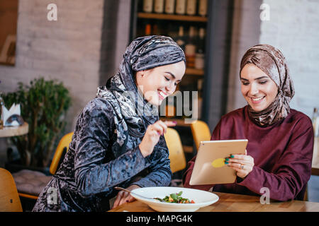 Due donne musulmane in cafe, shop online utilizzando la tavoletta elettronica Foto Stock