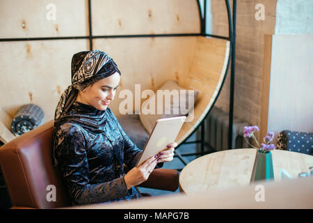 Bella arabo musulmano ragazza utilizzando tablet in cafe Foto Stock