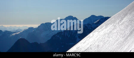 Un fantastico paesaggio di montagna panorama con un luccichio pendio di neve in primo piano e molte creste silhouette dietro Foto Stock