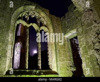 Una vista notturna attraverso una finestra ad arco guardando la luna al Fountains Abbey in North Yorkshire, Regno Unito. Foto Stock