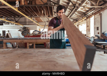 Falegname abilmente ispezionando un asse di legno nel suo laboratorio Foto Stock