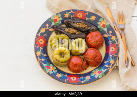 Vista superiore shot di carne ripieni pomodori, peperoni e melanzane in piastra colorata con ornamenti floreali su bianco sullo sfondo di legno con rame colore c Foto Stock