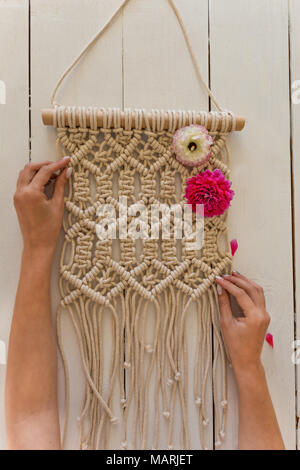 Artista mani macrame wall art con alcuni fiori di primavera su di esso. Foto Stock