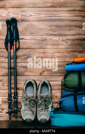 Stile di vita turistica con le scarpe da trekking, sacchi a pelo, tenda e pali trekking su sfondo di legno con copia spazio per il testo Foto Stock