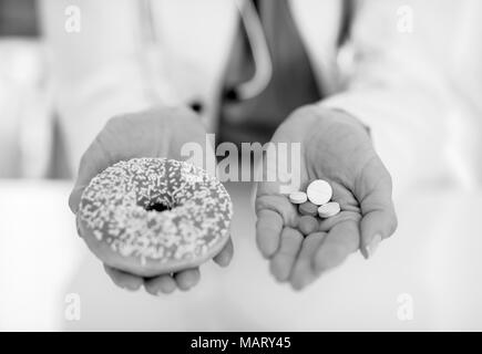 Primo piano sul medico donna che mostra a ciambella e pillole Foto Stock