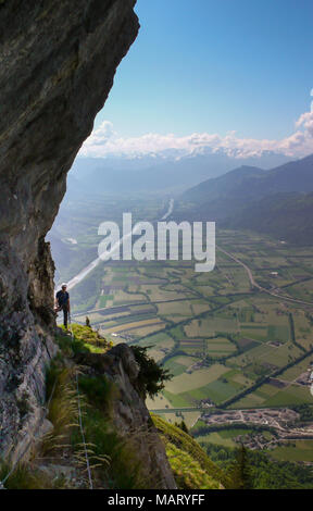 Maschio di rocciatore su un ripido ed esposto rock band sul suo modo di un percorso di arrampicata con una fantastica vista del paesaggio di montagna dietro di lui Foto Stock