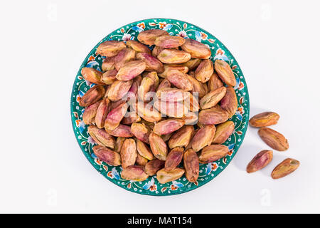 Vista superiore colpo di Fresco secco Grandi chicchi grezzi di Pistacchi di Bronte in un colore turchese piastra con design Persiano isolati su sfondo bianco, Bassa Calor Foto Stock