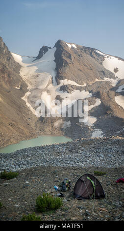 Camp alpina, tenda e marce, con montagne coperte di neve e di un lago glaciale in background. (Montagne litoranee, BC, Canada) Foto Stock