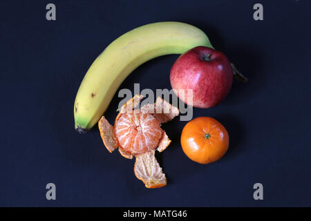 Banana, mela rossa e due piccole Arance, uno parzialmente pelato. Foto Stock