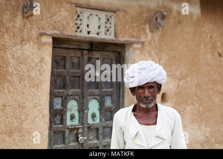 Uomo che indossa un turbante bianco al di fuori di un haveli tradizionale con una vecchia porta di legno in Mandawa, rurali Rajasthan, India.