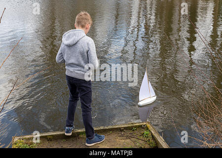 Un giovane ragazzo vele il suo yacht bianco sulle acque della fossa Ackers, Warrington, Cheshire, Inghilterra, Regno Unito il 03 aprile 2018 Foto Stock