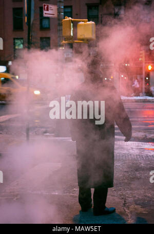 Un uomo che indossa una fedora in piedi su un steamy street a New York City. Foto Stock