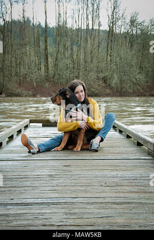 Una donna seduta con il suo cane su un dock in Oregon. Foto Stock