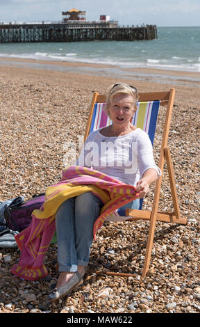 Donna seduta in una sedia a sdraio sulla spiaggia in una giornata di vento. Southsea, England Regno Unito Foto Stock