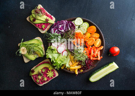 Colazione sana insalata e pane tostato con verdure e microgreen su sfondo scuro. Pulire mangiando la dieta vegetariana cibo sano concetto. Vista dall'alto. Foto Stock