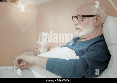 Senior uomo malato giacente e assunzione di pillole. Foto Stock