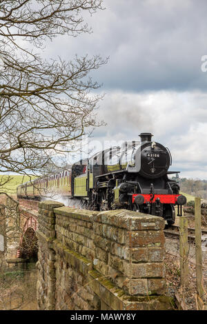 Vista frontale della vecchia, vintage SVR locomotiva a vapore 43106 (LMS Ivatt Classe 4) avvicinando, sbuffando fumo, viaggiando attraverso la paesaggistica campagna in primavera. Foto Stock