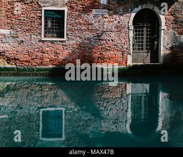 La facciata della parzialmente mossy vecchia casa di mattoni con vintage in legno porta in stretto canale a Venezia, Italia. Foto Stock