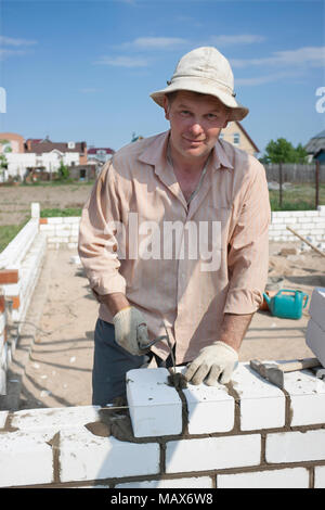 Muratore costruisce un muro di mattoni bianchi Foto Stock