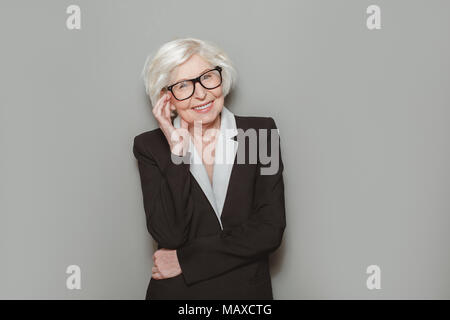 Le donne più anziane indossare tuta formale e occhiali studio isolato su sfondo guardando la telecamera sorridendo allegro gentile maestro Foto Stock