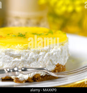 Ristorante di impostazione di una mousse al limone cheesecake una forcella d'argento su una piastra bianca di sfondo morbido con fiori di colore giallo e di inserzione spazio di copia Foto Stock