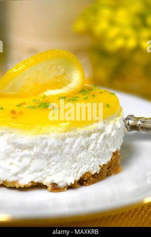 Ristorante di lusso di impostazione di una mousse al limone cheesecake una forcella d'argento su una piastra bianca di sfondo morbido con fiori di colore giallo e di inserzione spazio di copia Foto Stock