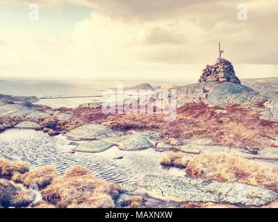 Picco di montagna in salita sulla piccola isola in Norvegia. Piramide sovrapposti in corrispondenza di spigoli cliff, blu oceano con riflessioni di sun. Inizio estate trail. Foto Stock