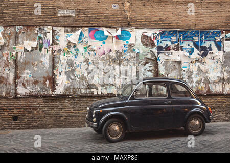 Un vecchio blu Fiat 500 parcheggiato in una acciottolata strada torna in Italia a Roma accanto ad alcuni vecchi manifesti pubblicitari. Foto Stock