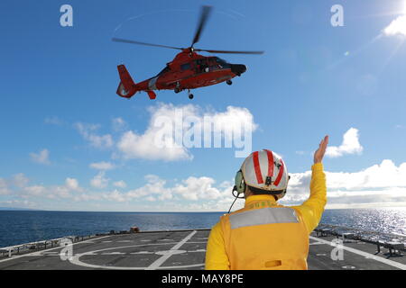 Un guardacoste Munro segnale di atterraggio officer, il Chief Petty Officer Benjamin Reedy, relè segnali ad una stazione di aria San Francisco equipaggio a bordo di un MH-65 Delfino elicottero durante un rifornimento verticale esercizio mentre la taglierina è stata disattivata la costa di Point Mugu, California, nov. 9, 2017. Un rifornimento verticale è un metodo per la consegna delle forniture, l'ingranaggio e attrezzature per frese in corso tramite elicottero. Stati Uniti La guardia costiera della foto. Foto Stock