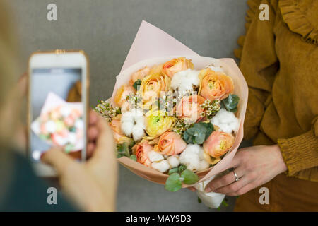 Ragazza tira sullo smartphone bellissimo bouquet rustico in amico le mani Foto Stock