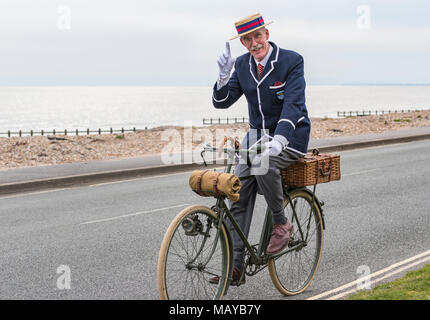 Uomo anziano in bicicletta su una bicicletta vittoriano vestito in costume che indossa un blazer e paglia navigante hat, NEL REGNO UNITO. Gentleman tipping hat. Foto Stock