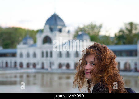 Carino redhead girl guardando la telecamera sorridendo con un bianco edificio barocco in background Foto Stock