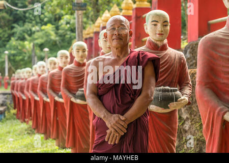 Älterer Mönch posiert vor einer Reihe Mönch-Statuen an der Kaw Ka Thaung Höhle di Hpa-an, Myanmar, Asien | anziani monaco in posa di fronte a una fila di mon Foto Stock