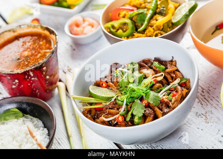 Asian pollo e curry di gamberi con riso e involtini primavera pezzi, servita su vecchie tavole di legno. Foto Stock