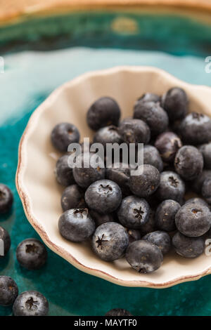 Mangiare sano. I mirtilli in piccoli e bianchi ceramice piastra. Profondità di campo. Composizione verticale. Foto Stock