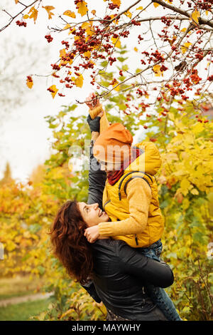 Famiglia autunno in autunno parcheggiare all'esterno. Felice madre aiutando il suo bambino Boy Foto Stock