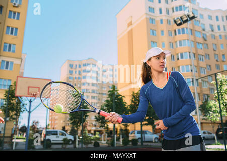 Donna giocando a tennis all'aperto, hot shot palla. La pratica del tennis sul campo da tennis a giornata di sole su un sfondo della città Foto Stock