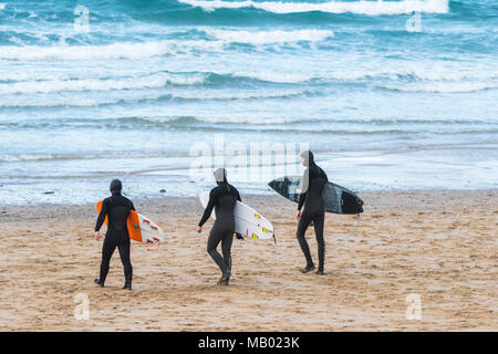 Tre i surfisti a piedi al mare su Fistral Beach in Newquay in Cornovaglia. Foto Stock