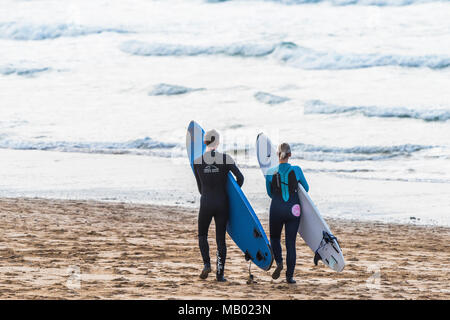 Due surfisti che trasportano i loro surboards e per raggiungere a piedi il mare su Fistral Beach in Newquay in Cornovaglia. Foto Stock