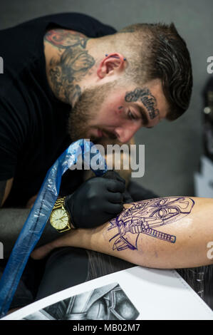 Luca Rudden tatuaggio un disegno sulla gamba di un maschio di cliente al Cornwall Tattoo Convention. Foto Stock